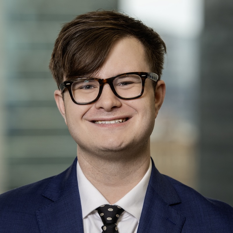 A headshot photograph of me. I am wearing a gray suit, a black tie, and glasses. The background is the six columns on MU's Francis Quadrangle.